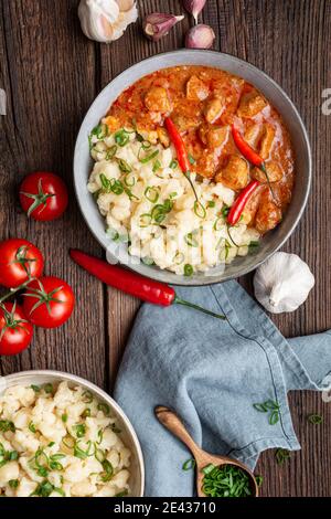 Stufato di maiale caldo con peperoncino, servito con gnocchi lessati con cipollotti su rustico fondo di legno Foto Stock