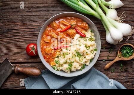 Stufato di maiale caldo con peperoncino, servito con gnocchi lessati con cipollotti su rustico fondo di legno Foto Stock