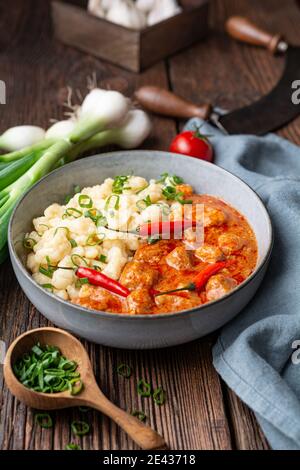 Stufato di maiale caldo con peperoncino, servito con gnocchi lessati con cipollotti su rustico fondo di legno Foto Stock