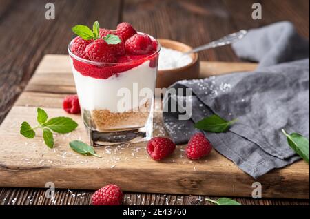 Non cuocere il dessert alla cheesecake in un recipiente di vetro con il coperchio purea di lamponi e bacche fresche su rustico sfondo di legno Foto Stock