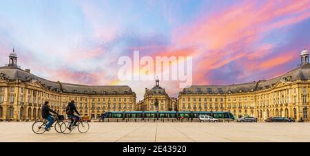 Due ciclisti vicino a Place de la Bourse e un tram alla sua stazione, a Bordeaux in Nuova Aquitania, Francia Foto Stock