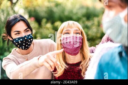 Giovani multirazziali che si divertono insieme indossando maschera facciale - Nuovo concetto di stile di vita normale con amici felici che condividono il tempo libero fuori al parco Foto Stock