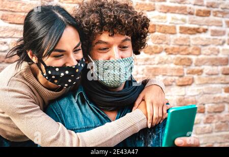 Giovane coppia innamorata guardando il cellulare smartphone indossando il viso Maschera - nuovo concetto di tecnologia normale con l'uomo e la donna in attesa di buone notizie sul blocco Foto Stock