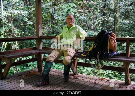 escursionista maschile di media età che riposa in una foresta pluviale tropicale in un'area di riposo coperta Foto Stock