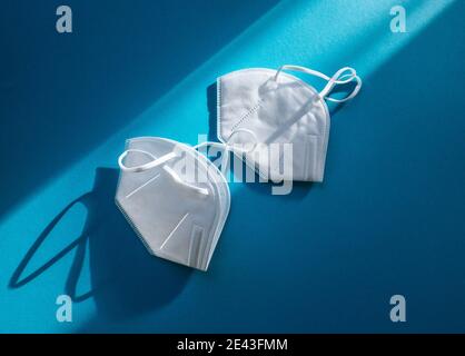 Due maschere facciali FFP2 per uso medico bianche isolate su colore blu sfondo Foto Stock