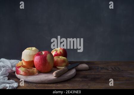 Mele rosse fresche mature intere e tagliate a fette con tagliere e coltello disposto su rustico tavolo di legno Foto Stock