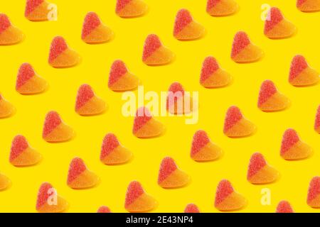 Vista dall'alto piatto composizione di caramelle in gelatina multicolore forma del cuore disposta in righe su sfondo giallo Foto Stock