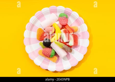 Vista dall'alto delle caramelle gommoso multicolore su piatto a righe posizionato su sfondo giallo Foto Stock