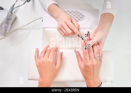 Dall'alto di raccolto anonimo maestro con elegante manicure esame unghie di cliente femminile mentre lavora in salone di bellezza Foto Stock