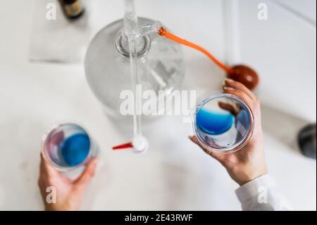 Dall'alto di raccolto anonimo scienziato con becher con blu liquido in mano che conduce esperimenti chimici mentre lavora su nuovo formula per il farmaco Foto Stock