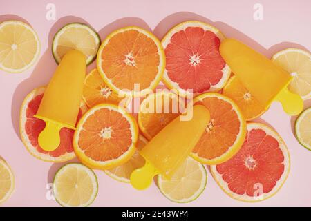 Frutta di ghiaccio arancio e fette di arancia, lime e pompelmo su sfondo rosa. Vista dall'alto. Foto Stock