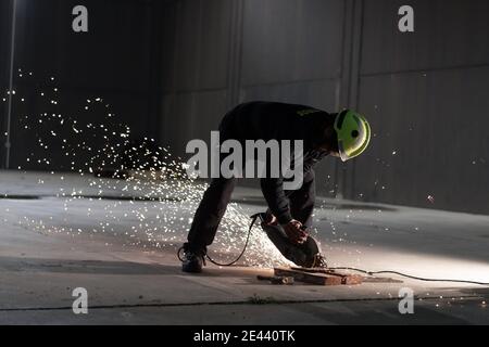 Corpo completo di saldatore maschio irriconoscibile in casco protettivo e. occhiali di protezione per tagliare i dettagli del ferro con taglierina durante il lavoro fabbrica industriale di notte Foto Stock