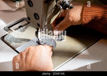 Alto angolo di raccolto seamstress senior senza volto mettendo filo in macchina da cucire in officina Foto Stock