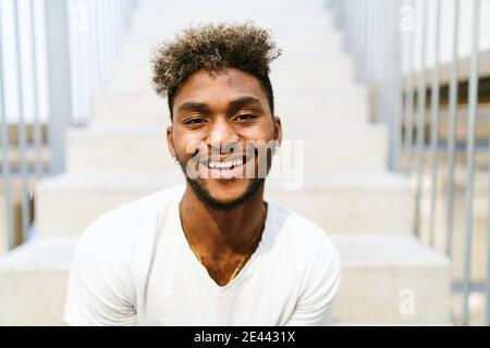 Bel ragazzo nero hipster con i capelli ricci vestito in una camicia bianca casual che guarda la macchina fotografica Foto Stock
