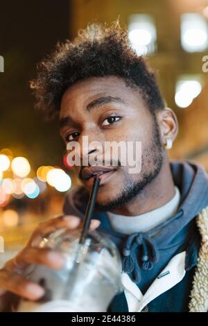 Positivo giovane africano americano hipster maschio con capelli ricci e. la barba indossa una giacca calda guardando la fotocamera e sorridendo amichevole mentre si è di nuovo in piedi Foto Stock