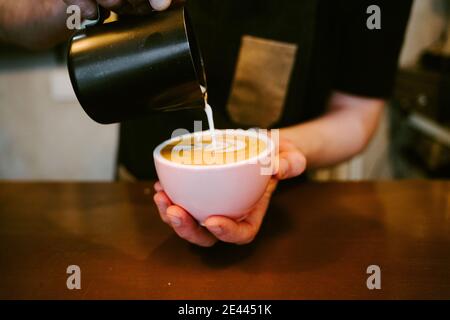 Primo piano di un cameriere che serve il latte a una tazza di caffè Foto Stock