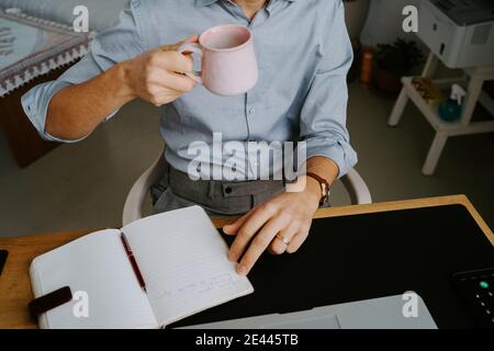 crop imprenditore maschio che ha videoconferenza su laptop e bere bevande calde mentre discutono i problemi di lavoro con i colleghi durante il coronavirus panoramica Foto Stock