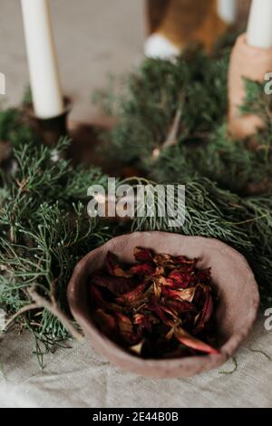 Composizione natalizia con ciotola rustica in legno ripiena di rosso secco petali di fiori disposti vicino a rami di abete verde e candele su tabella Foto Stock
