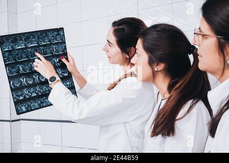 Medico in un cappotto bianco in uniforme che mostra una radiografia ad altri due medici in una stanza di ospedale Foto Stock
