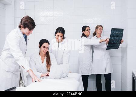 Un gruppo di medici che lavorano su un computer portatile mentre due Le dottoresse esaminano i raggi X in una stanza bianca dell'ospedale Foto Stock