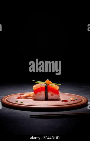 Appetitosi sushi nigiri con salmone e gamberi serviti a turno tavola di legno sul tavolo con bastoncini su sfondo nero Foto Stock