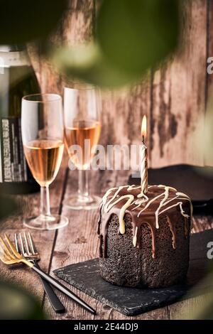 Deliziosa torta al cioccolato con candela bruciante servita su tavola di ardesia sul tavolo con bicchieri di champagne al caffè Foto Stock