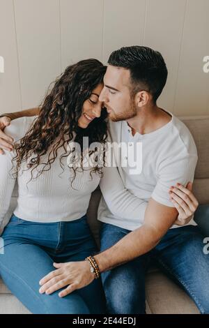 Coppia amorevole seduta su morbido divano e teneramente abbracciando mentre goditi il weekend insieme a casa tua Foto Stock