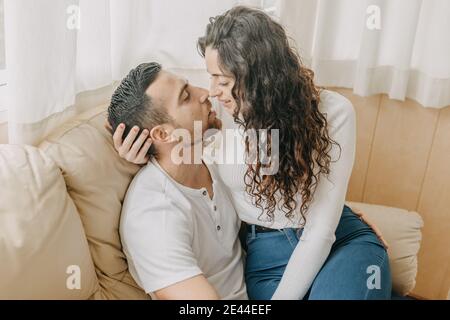 Coppia amorevole seduta su morbido divano e teneramente abbracciando mentre goditi il weekend insieme a casa tua Foto Stock