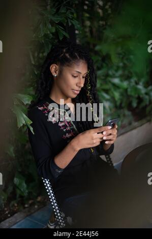 Giovane attraente afroLatina Donna utilizzando uno smartphone, vista profilo Foto Stock