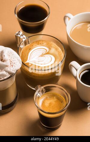 Set di diversi tipi classici di bevande aromatiche al caffè serviti in tazze di varie misure disposte su superficie beige Foto Stock