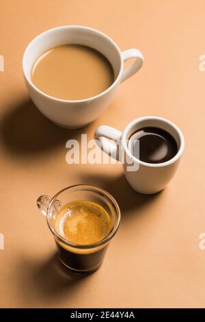 Set di diversi tipi classici di bevande aromatiche al caffè serviti in tazze di varie misure disposte su superficie beige Foto Stock