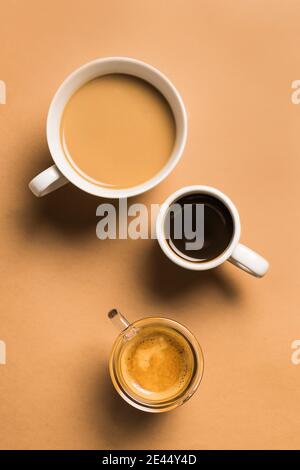 Set di diversi tipi classici di bevande aromatiche al caffè serviti in tazze di varie misure disposte su superficie beige Foto Stock