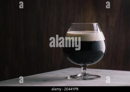 Vetro di cristallo di birra scura stout posto tavolo in marmo bar Foto Stock