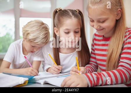 Tre belle shoolgirl che chiacchierano durante la lezione di disegno della scuola elementare. Bella bambina che guarda il suo amico sketching. Educazione, amicizia Foto Stock