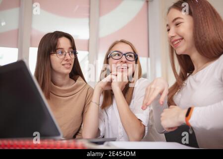 Gruppo di teen studentesse che parlano durante la lezione. Belle ragazze adolescenti che discutono il loro progetto, utilizzando il laptop in classe. Educazione, amicizia, tecnologia Foto Stock