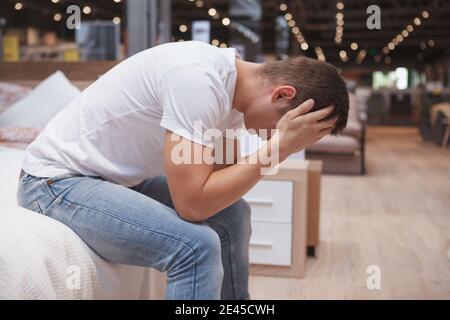 Uomo seduto su un letto con il volto in lui mani che si sentono solitarie e depresse Foto Stock