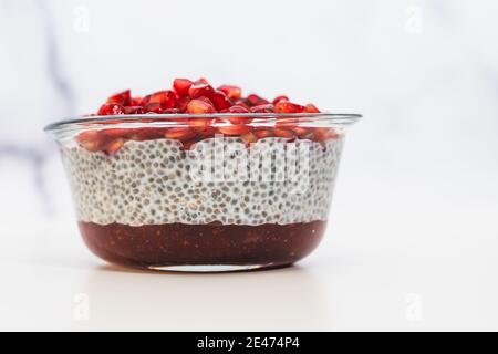 Budino di semi di Chia con marmellata di lamponi e semi di melograno il recipiente in vetro si avvicina su sfondo bianco Foto Stock