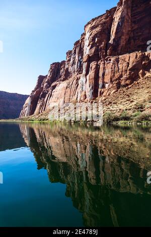 Le pareti in arenaria rossa e illuminata con luce brillante all'interno del Glen Canyon si riflettono nella superficie limpida e tranquilla del possente fiume Colorado vicino a Page, Arizona. Foto Stock