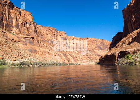 L'interno del Glen Canyon visto dalla superficie del fiume Colorado con pareti di arenaria illuminate e un cielo blu chiaro. Foto Stock