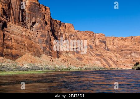 L'interno del Glen Canyon visto dalla superficie del fiume Colorado con pareti di arenaria illuminate e un cielo blu chiaro. Foto Stock