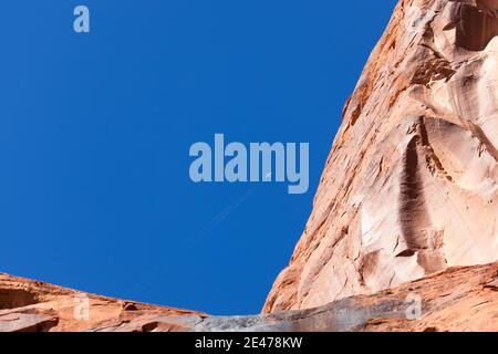 Alte pareti di arenaria in Glen Canyon contro un cielo blu vibrante con un aereo che sembra piccolo in contrasto. Foto Stock
