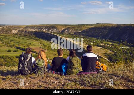 Sognante gruppo di giovani escursionisti seduti sul bordo della montagna e guardando in lontananza. Foto Stock