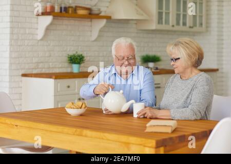 Felice coppia senior nonni seduti in cucina, bere tè con biscotti Foto Stock