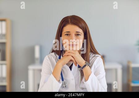Ritratto di una giovane dottoressa con capelli rossi stanchi seduta al tavolo e appoggiata alle mani. Foto Stock