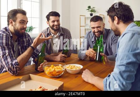 Gruppo di uomini sorridenti amici seduti con bottiglie di orso e. spuntini e chiacchiere Foto Stock