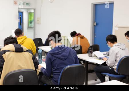 Gli studenti con maschera facciale leggono e fanno corsi in aula In università a Hong Kong durante il Covid-19 Foto Stock
