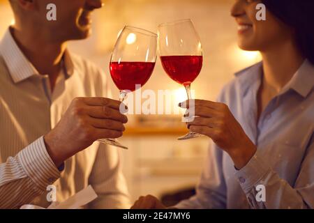 Uomo e donna innamorati gustando vino rosso e clinking bicchieri in serata romantica a casa Foto Stock