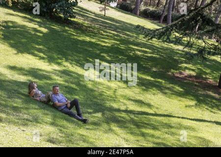 Coppia di mezza età che giace su erba verde su una collina e. parlare Foto Stock