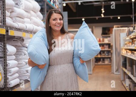 Donna allegra e attraente sorridente, che ha riposto due cuscini, che acquista articoli per la casa Foto Stock