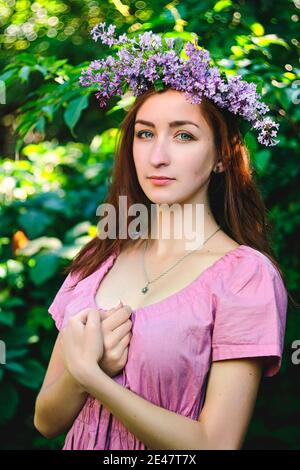 Ritratto di giovane bella donna in abito rosa in giardino primaverile con lilla. Sfondo della molla. Giorno della donna. Biglietto d'auguri. Foto Stock